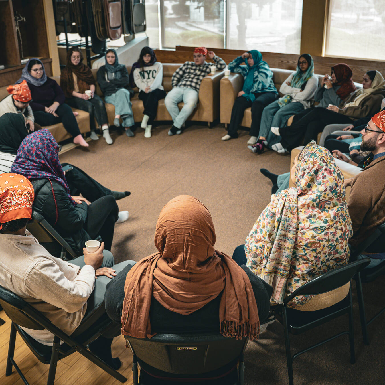 A group of students and facilitators, all wearing headscarves, sitting in a circle and talking.